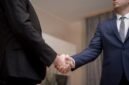 Dua tangan berjabat erat di latar belakang gedung pencakar langit modern, melambangkan momen penting dalam sebuah kesepakatan akuisisi atau merger perusahaan yang mengubah lanskap bisnis. Gambaran ini menangkap esensi kolaborasi strategis di dunia korporat yang dinamis dan penuh tantangan.