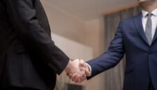 Dua tangan berjabat erat di latar belakang gedung pencakar langit modern, melambangkan momen penting dalam sebuah kesepakatan akuisisi atau merger perusahaan yang mengubah lanskap bisnis. Gambaran ini menangkap esensi kolaborasi strategis di dunia korporat yang dinamis dan penuh tantangan.