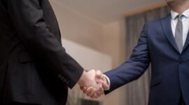 Dua tangan berjabat erat di latar belakang gedung pencakar langit modern, melambangkan momen penting dalam sebuah kesepakatan akuisisi atau merger perusahaan yang mengubah lanskap bisnis. Gambaran ini menangkap esensi kolaborasi strategis di dunia korporat yang dinamis dan penuh tantangan.
