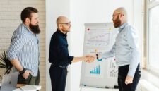 Dua pebisnis berjabat tangan di depan grafik pertumbuhan yang melambangkan keberhasilan merger, menunjukkan sinergi dan optimisme terhadap masa depan yang lebih kuat. Integrasi strategis ini bertujuan menciptakan entitas bisnis yang lebih besar dan berdaya saing di tengah dinamika ekonomi.