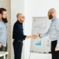 Dua pebisnis berjabat tangan di depan grafik pertumbuhan yang melambangkan keberhasilan merger, menunjukkan sinergi dan optimisme terhadap masa depan yang lebih kuat. Integrasi strategis ini bertujuan menciptakan entitas bisnis yang lebih besar dan berdaya saing di tengah dinamika ekonomi.