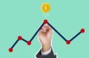 Ilustrasi tangan memegang uang tunai dengan latar belakang grafik pasar saham, menggambarkan potensi keuntungan dari investasi dan pembagian dividen. Gambar ini merepresentasikan kesuksesan finansial yang dapat diraih melalui keputusan investasi yang tepat.