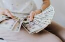 Tangan memegang tumpukan uang tunai, menggambarkan aliran dana dividen yang mengalir langsung ke tangan investor, sebagai bentuk keuntungan dari kepemilikan saham perusahaan. Momen ini menjadi tanda positif bagi kesehatan finansial perusahaan dan hadiah bagi kesabaran investor.