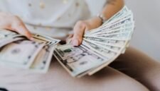 Tangan memegang tumpukan uang tunai, menggambarkan aliran dana dividen yang mengalir langsung ke tangan investor, sebagai bentuk keuntungan dari kepemilikan saham perusahaan. Momen ini menjadi tanda positif bagi kesehatan finansial perusahaan dan hadiah bagi kesabaran investor.