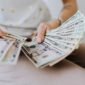 Tangan memegang tumpukan uang tunai, menggambarkan aliran dana dividen yang mengalir langsung ke tangan investor, sebagai bentuk keuntungan dari kepemilikan saham perusahaan. Momen ini menjadi tanda positif bagi kesehatan finansial perusahaan dan hadiah bagi kesabaran investor.
