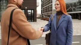 Tangan-tangan profesional berjabatan di tengah hiruk pikuk kota yang modern, merefleksikan kompleksitas dan dampak luas dari sebuah keputusan aksi korporasi yang dapat mengubah lanskap bisnis dan kehidupan banyak orang. Di sisi lain, terlihat pula gambaran masyarakat yang aktif di media sosial, menunjukkan bagaimana teknologi dan keputusan korporasi memengaruhi interaksi sehari-hari.
