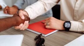 Dua pebisnis berjabat tangan di atas latar belakang gedung pencakar langit kota, melambangkan kesepakatan merger yang strategis untuk mencapai tujuan bisnis yang lebih besar. Penggabungan ini diharapkan membawa sinergi dan pertumbuhan signifikan bagi kedua belah pihak.